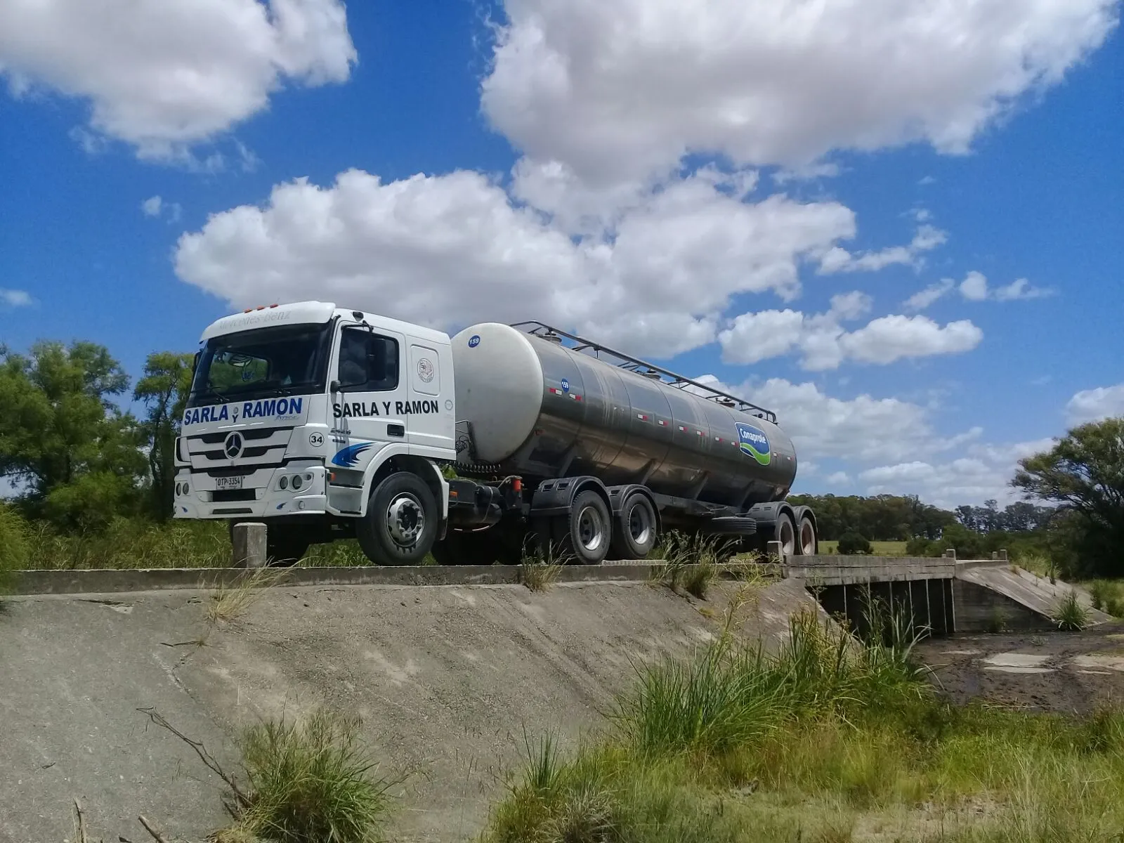 Camión cisterna de Sarla y Ramón con tanque térmico de Conaprole cruzando un puente rural