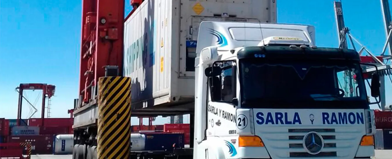 Camión de Sarla y Ramón en el puerto mientras una grúa carga un contenedor refrigerado sobre el chasis
